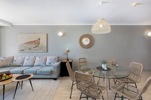 A modern living room with a sofa, dining table, chairs, a hanging light fixture, and a wall-mounted mirror.