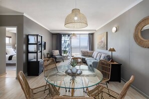 A modern living room with a glass-top coffee table, wicker chairs, a sofa, and a large window offering a view.