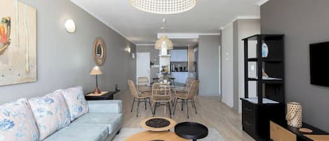 A modern living room with a sofa, dining table, chairs, and a TV.