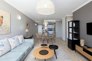 A modern living room with a sofa, dining table, chairs, and a TV.