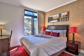 Une chambre d’hôtel avec un grand lit, deux lampes de chevet, une vue sur la ville et une moquette rouge à motifs.