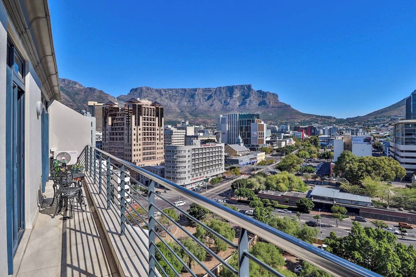 A cityscape with modern buildings, a clear blue sky, and a mountain in the background.