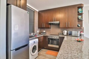 Une cuisine compacte équipée d’un réfrigérateur en acier inoxydable, d’un lave-linge, d’un four à micro-ondes et d’un four encastré.