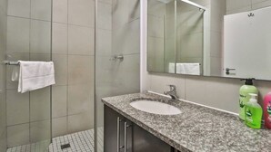 A bathroom with a shower, a sink, a mirror, and a towel rack. - Quayside 1206 by Ctha (Cape Town)