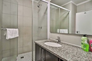 Un bagno con doccia, lavandino, specchio e porta asciugamani.