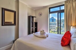 Una camera d'albergo con un letto, un cuscino rosso, una sveglia e una finestra vista città.