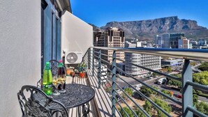 A balcony with a table, potted plants, and a view of a cityscape and mountain. - Quayside 1206 by Ctha (Cape Town)