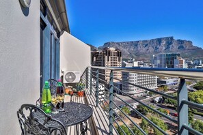 Un balcone con un tavolo, piante in vaso e vista sulla città e sulle montagne.