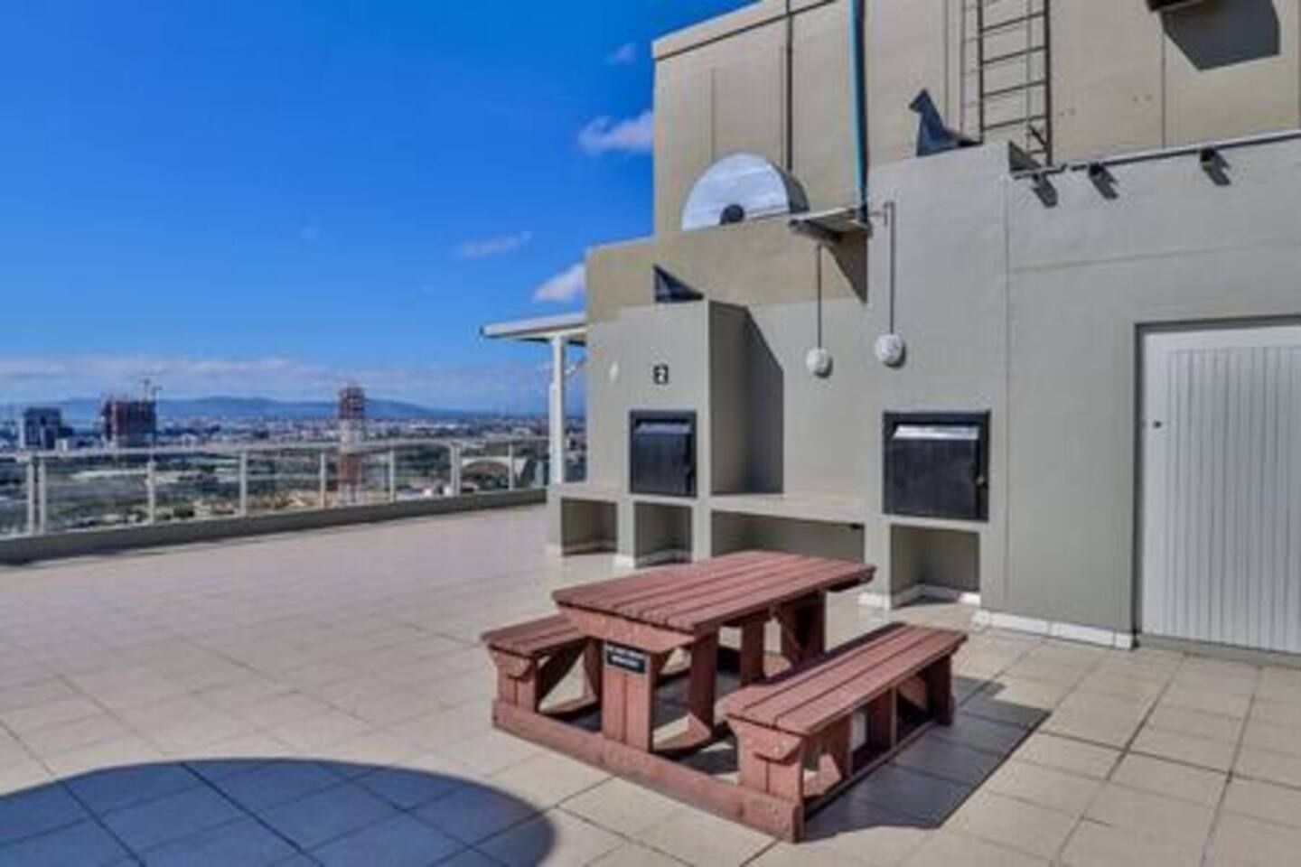 A rooftop terrace with a wooden picnic table and a view of the cityscape.