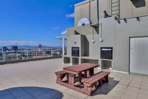 A rooftop terrace with a wooden picnic table and a view of the cityscape.