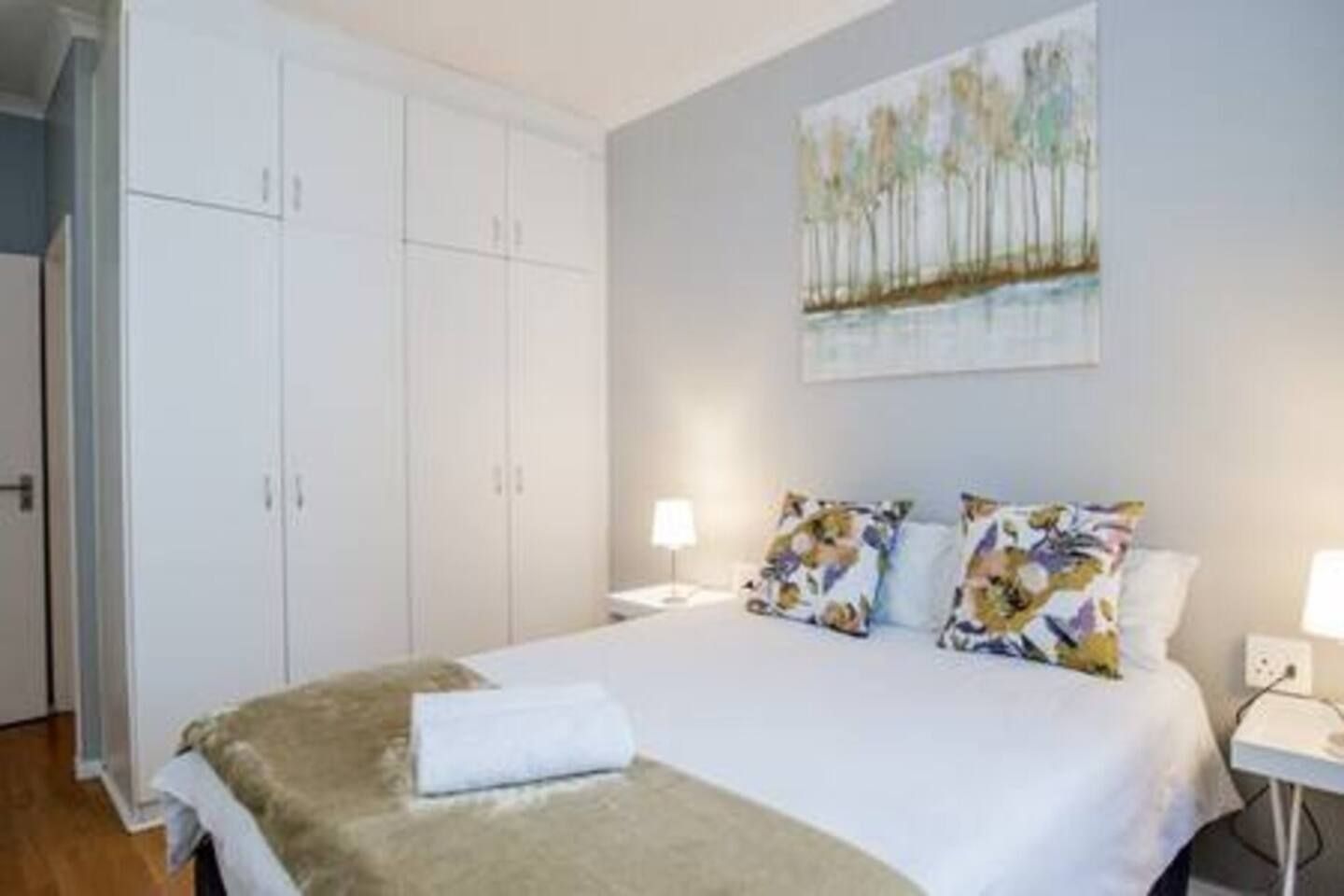 Quarto com cama, duas mesas de cabeceira, um guarda-roupa e um quadro na parede.
