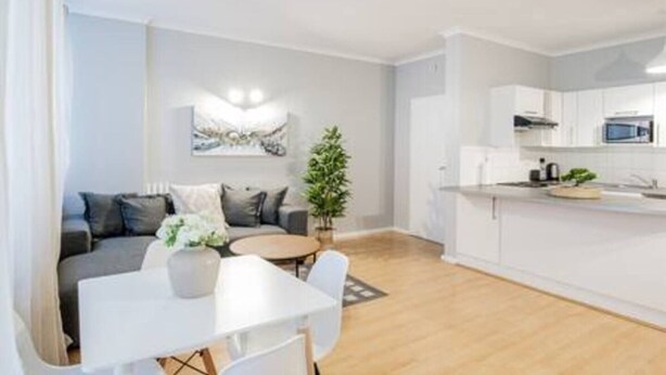 Un apartamento moderno con comedor, sala de estar con sofá, cocina con armarios blancos y una planta en maceta.