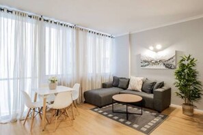 Un salon moderne avec un canapé gris, une table basse ronde et un coin repas comprenant une table et des chaises blanches.