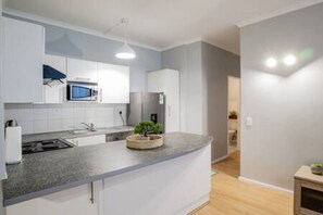 A modern kitchen with white cabinets, a granite countertop, a microwave, and a small plant.