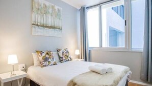 Habitación de hotel con cama, dos lámparas de noche, una ventana con cortinas y un cuadro en la pared.