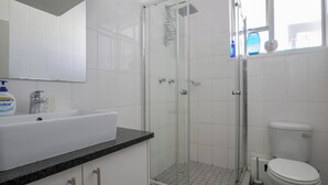 Et badeværelse med en hvid vask, en glasbrusekabine og et toilet.