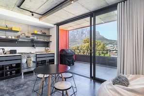 A modern kitchen with a dining area, a large sliding glass door to a balcony, and a view of a mountain.