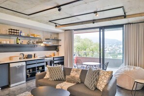 A modern living room with a sofa, a dining table, and a kitchen area with appliances. - Bo-kaap Hideaway | Pool & backup power by Ctha (Cape Town)