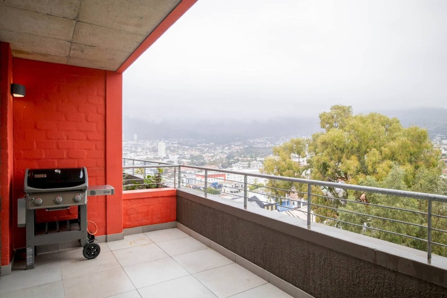 Een balkon met een barbecue, een rode bakstenen muur en een uitzicht op een stadsgezicht.