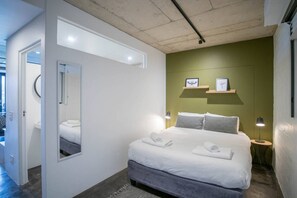 A modern bedroom with a large bed, bedside lamps, a mirror, and a view of the outdoors.