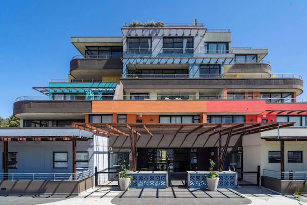 A multi-story hotel with a modern architectural design, featuring balconies, a covered entrance, and potted plants.