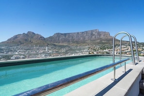A rooftop pool with a clear view of a mountain and a cityscape.