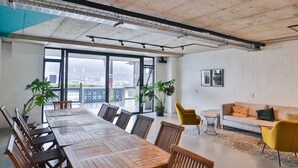 Ein moderner Büroarbeitsplatz mit großem Holztisch, gelben Stühlen, einer Couch und Topfpflanzen.