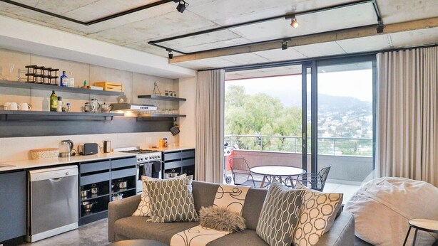 Eine moderne Küche mit eingebauten Geräten, ein Essbereich mit rundem Tisch und Stühlen sowie ein Balkon mit Blick auf die Stadt.