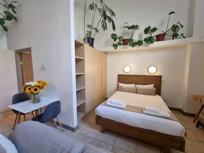 A hotel room with a bed, bedside tables, a desk with a chair, a vase of sunflowers, and potted plants.