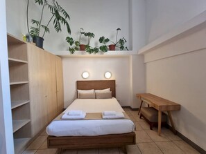A compact hotel room with a bed, bedside table, and built-in wardrobe. - Stylish City Studio | High ceilings & gym by Ctha (Cape Town)