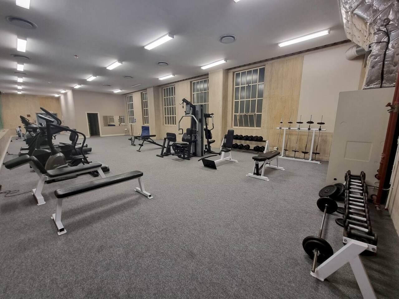 Ein Fitnessraum mit verschiedenen Trainingsgeräten, darunter Bänke, Kraftgeräte und Kurzhanteln.