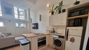 A compact kitchen with a washing machine, a microwave, and a refrigerator. There is a sofa and a TV in the living area.