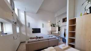 A modern, well-lit room with a sofa, a bed, a TV, and a kitchenette. - Stylish City Studio | High ceilings & gym by ctha (Cape Town)