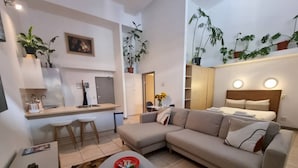 A modern living room with a sofa, a coffee table, and a dining area with chairs. - Stylish City Studio | High ceilings & gym by ctha (Cape Town)