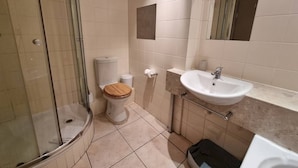 A bathroom with a glass-enclosed shower, a toilet with a wooden seat, a sink, and a mirror. - Stylish City Studio | High ceilings & gym by ctha (Cape Town)