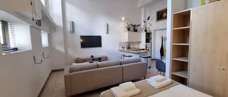 Una habitación moderna y luminosa con sofá, cama, televisor y kitchenette.