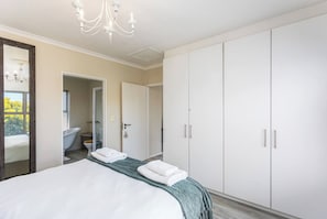 A hotel bedroom with a large bed, a wardrobe, a bathroom with a bathtub, and a chandelier.
