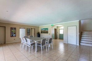 A spacious room with a large dining table, chairs, a painting on the wall, and a staircase.