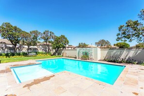 A rectangular swimming pool with a stone border, surrounded by a paved patio.