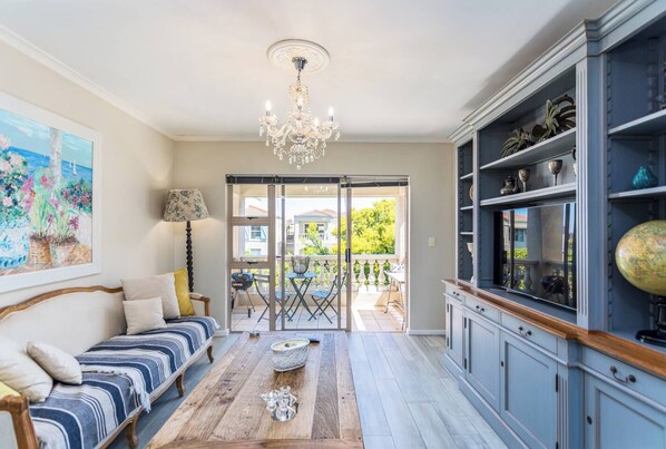 A living room with a sofa, a coffee table, a chandelier, and a view of the outside.