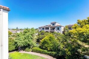 A two-story house with a balcony, surrounded by lush greenery and a clear blue sky.