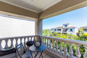 A balcony with a view of a residential building, a grill, and a chair.