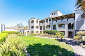 A multi-story residential building with balconies, a paved walkway, and landscaped gardens.