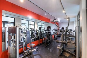 A gym with various exercise machines, large windows, and a red accent wall.