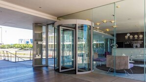 Ein moderner Hotelzugang mit einer Drehtür, Glasfassaden und einer Sitzecke mit gemusterten Kissen.