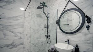 Un baño moderno con un lavabo blanco grande, un espejo redondo y un cabezal de ducha de mano.