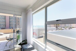 Un balcón con vistas al mar, una silla, una planta en maceta y una ventana con cortina.