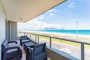 Un balcon meublé avec des meubles en osier, donnant sur une plage et une route.