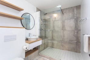 Un bagno moderno con doccia a vetro, uno specchio rotondo e un lavandino bianco.