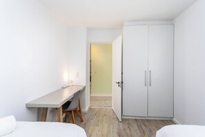 Une petite chambre moderne, équipée d’un lit, d’un bureau et d’une armoire.